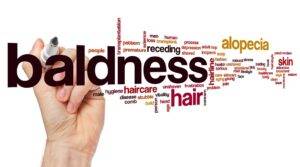 A graphic of a hand holding a marker writing the word "baldness" surrounded by related terms like "haircare," "alopecia," and "male pattern baldness" in various fonts and