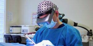 A dentist wearing a surgical mask and a magnification headlamp concentrates on a dental procedure in a clinic, surrounded by medical equipment, specializing in female hair loss.